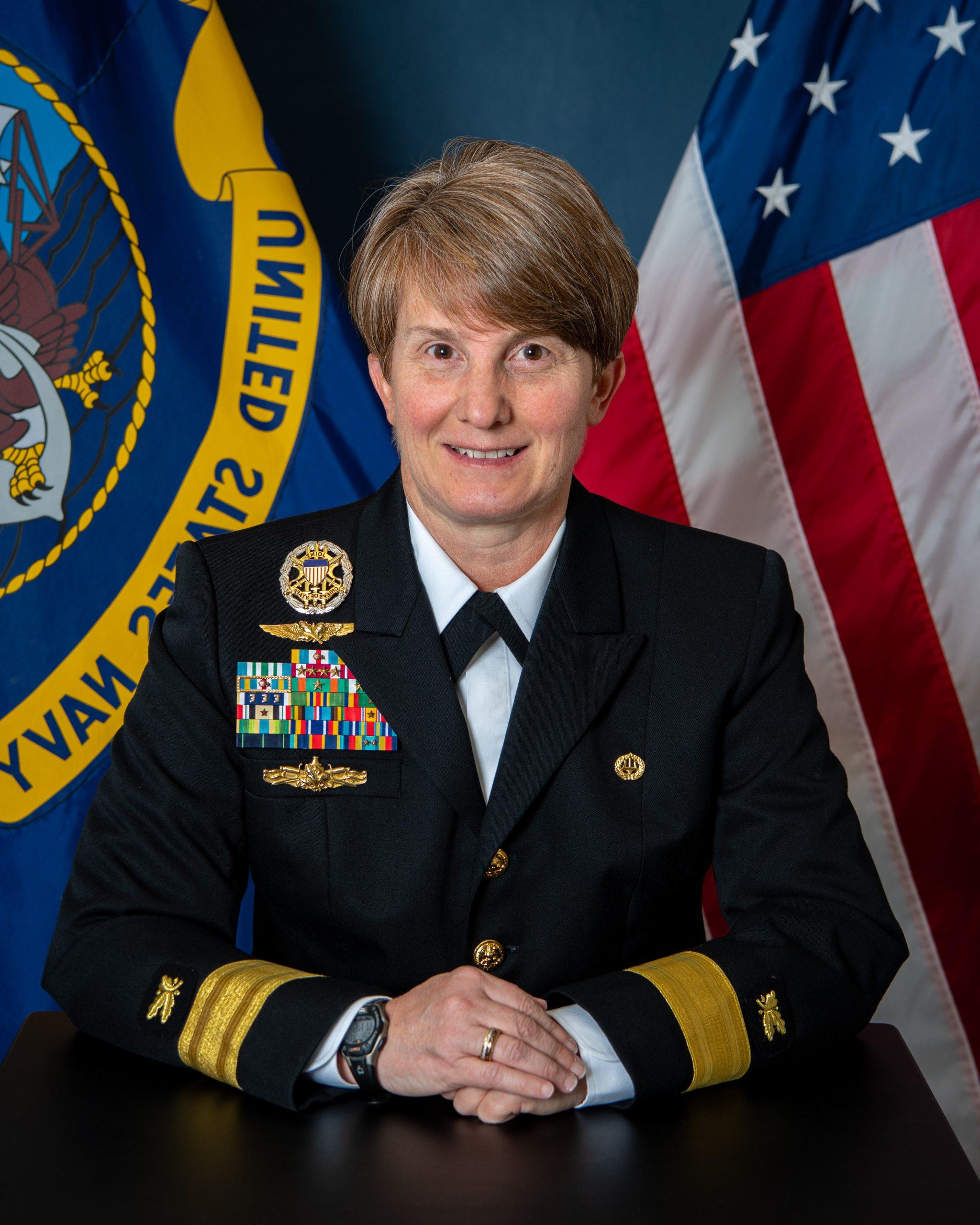 Portrait photo of Kristin Acquavella wearing her uniform against a backdrop of the United States and Naval flags.