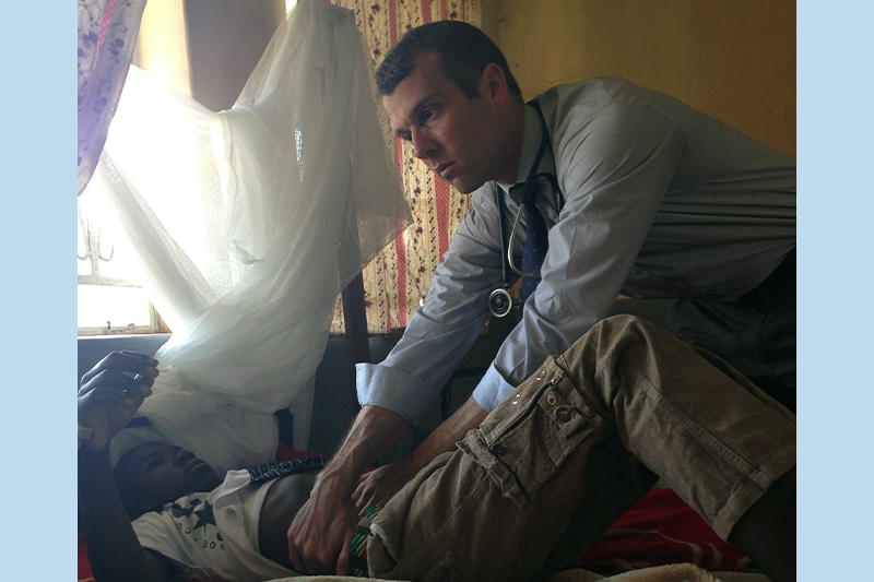 Dr. Ross Boyce tending to a child patient lying in a bed in Uganda.